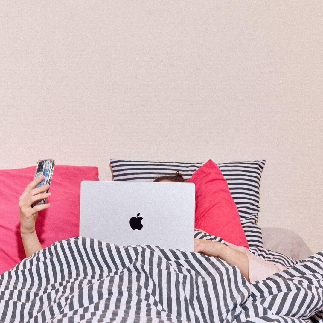 femme dans un lit avec un ordinateur et un smartphone