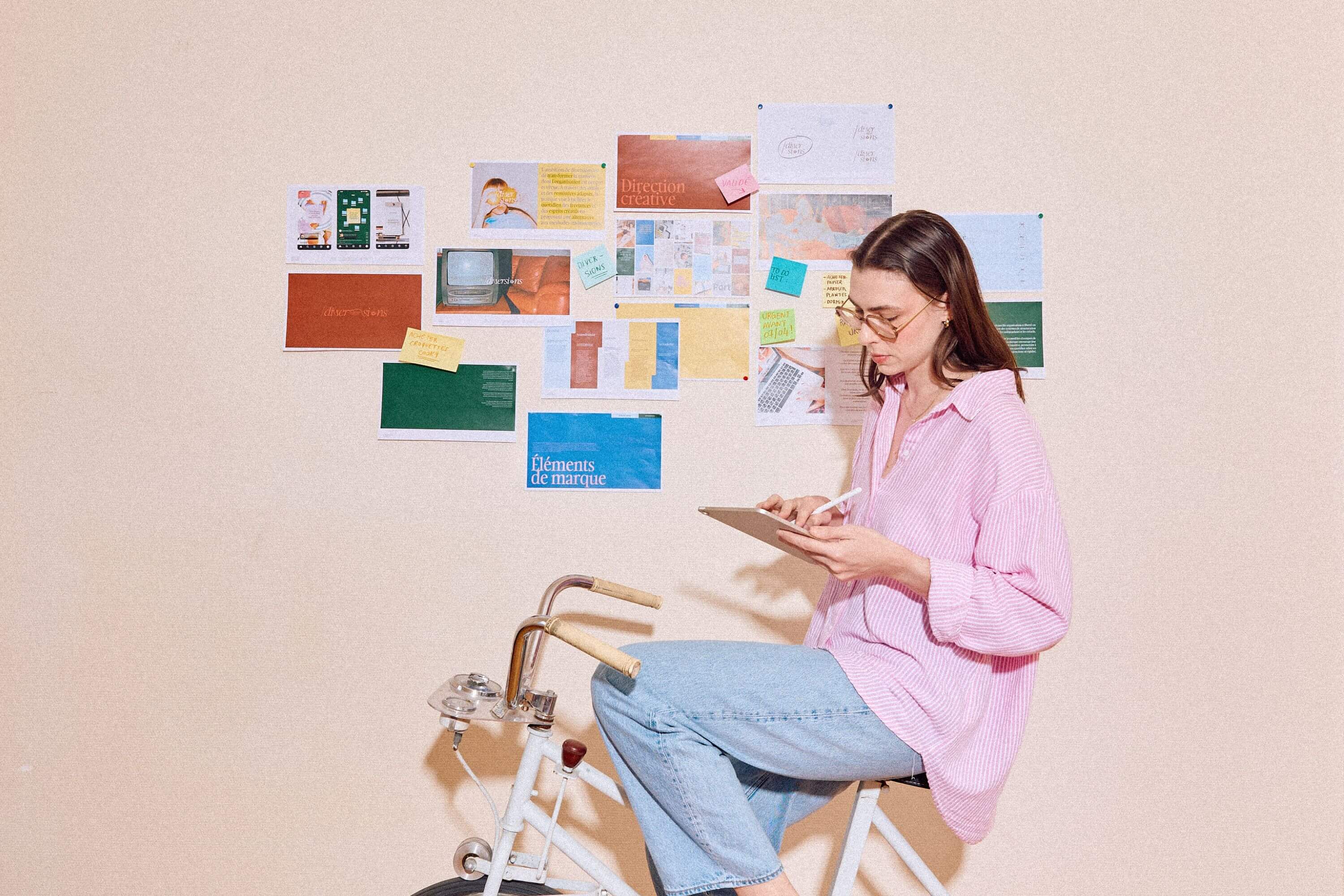 femme en chemise rose sur un vélo d'appartement vintage, écrivant sur une tablette