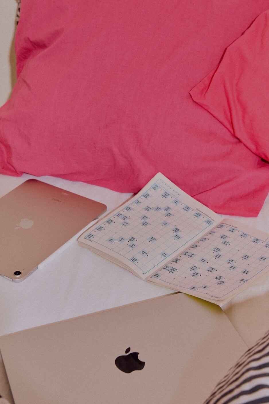 mots fléchés, ordinateur et tablette sur un lit