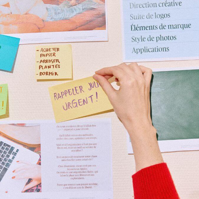 main plaçant un post-it sur un mur couvert de documents divers