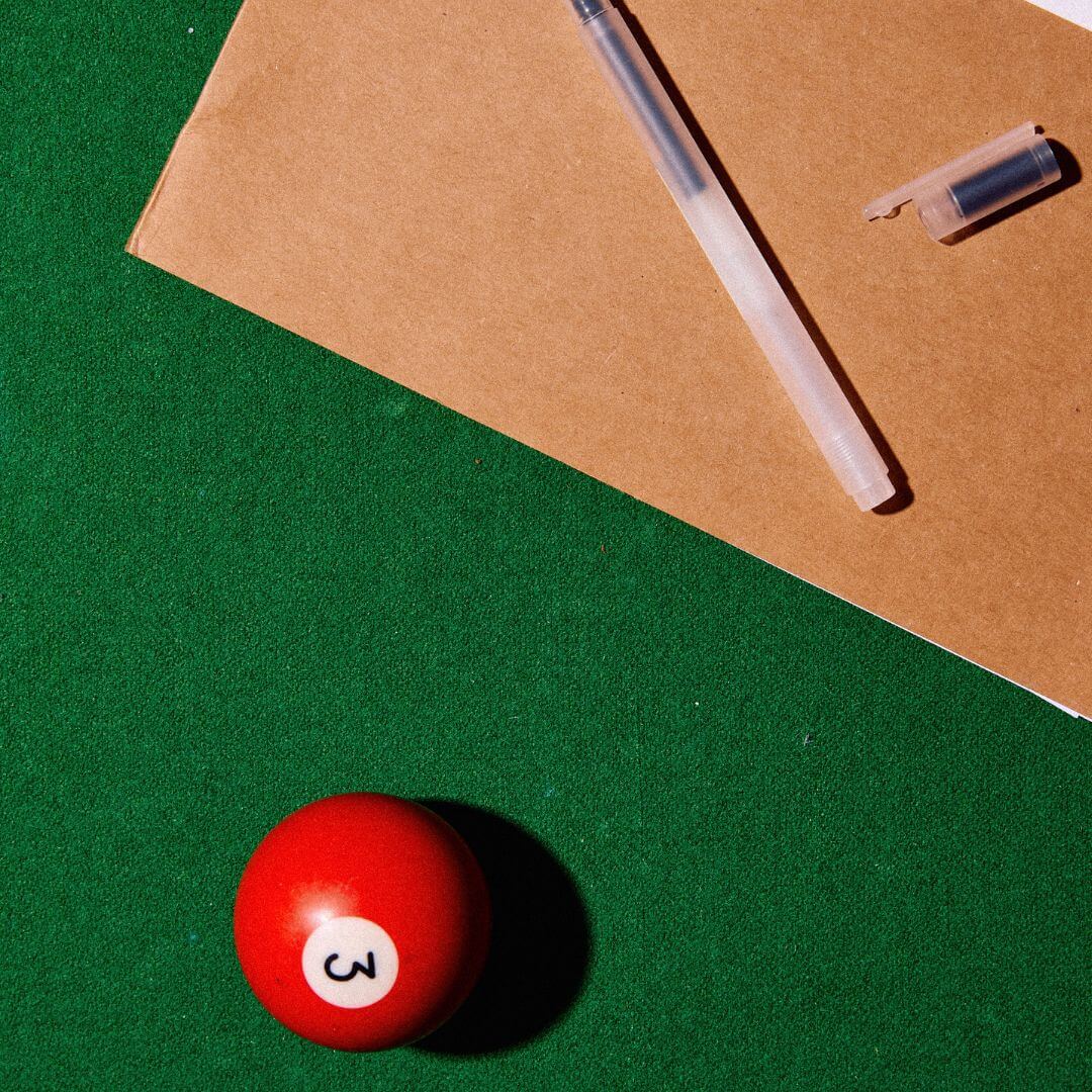 dossier et stylo posés sur une table de billard avec une boule de billard