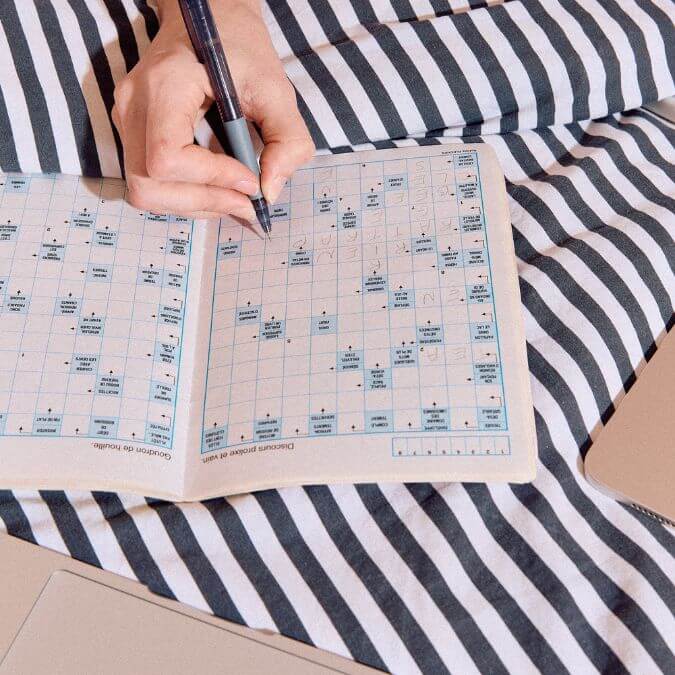 main en train de remplir une grille de mots fléchés