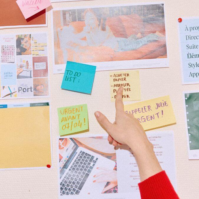 mains pointant un post it parmi différents papiers accrochés à un mur